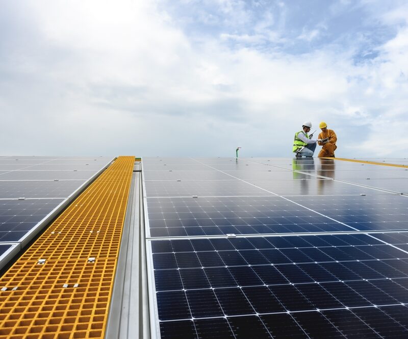 Two workers in safety gear are inspecting a large solar panel installation under a cloudy sky - Solar roof