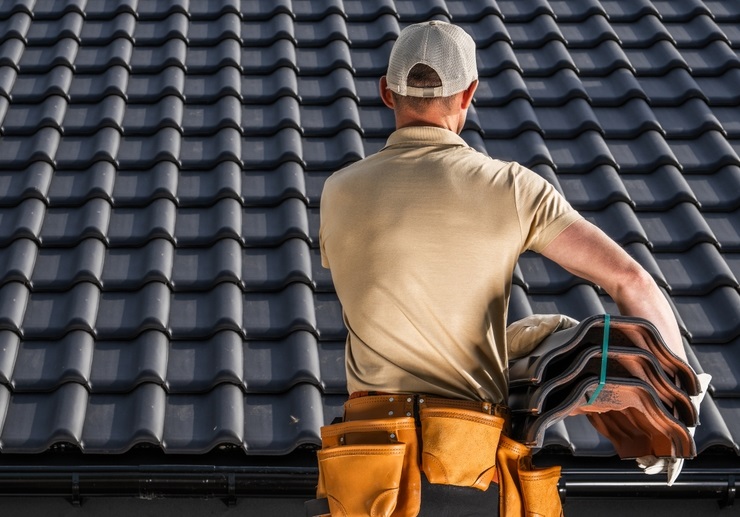 Skilled roofing professional carrying stacked roof tiles during a residential roofing project using premium materials – Roofing Supply San Diego.