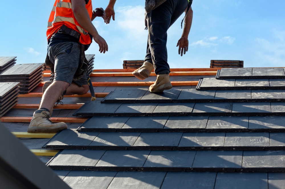 Skilled roofing contractors placing slate-style roof tiles with precision, showcasing durable materials designed for strength and longevity - Roofing Materials in San Diego.